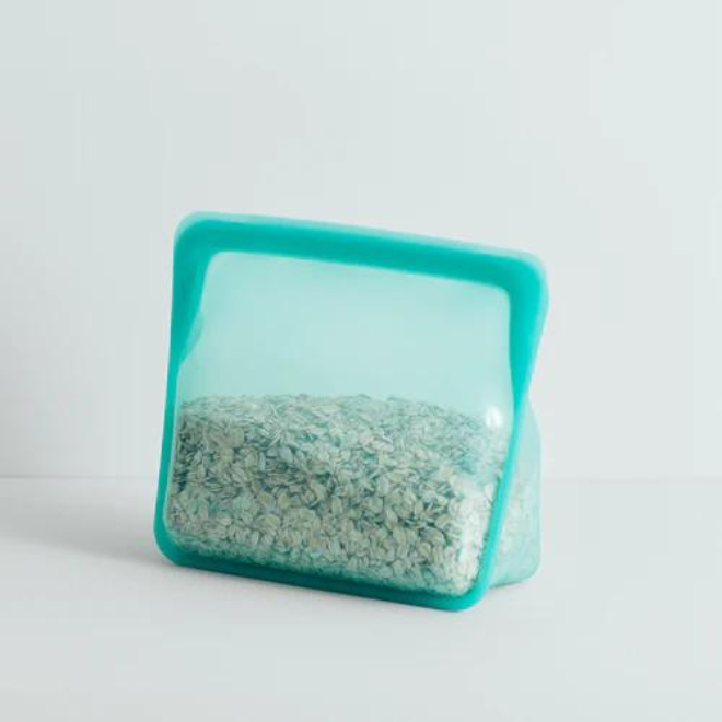 An aqua blue translucent standup silicone bag half-filled with rolled oats with a white background.